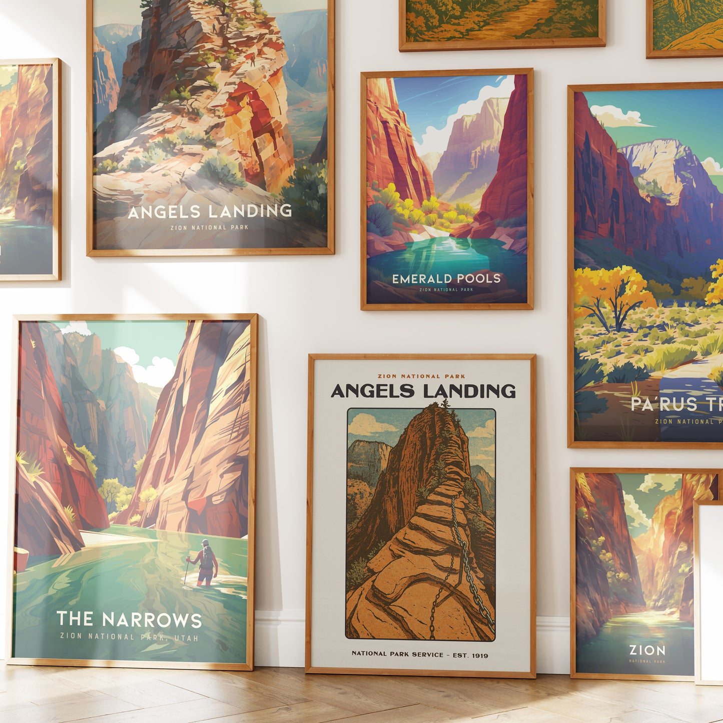 A collection of colorful prints featuring iconic landscapes from Zion National Park, including Angels Landing, Emerald Pools, and The Narrows, displayed in elegant wooden frames on a bright wall.