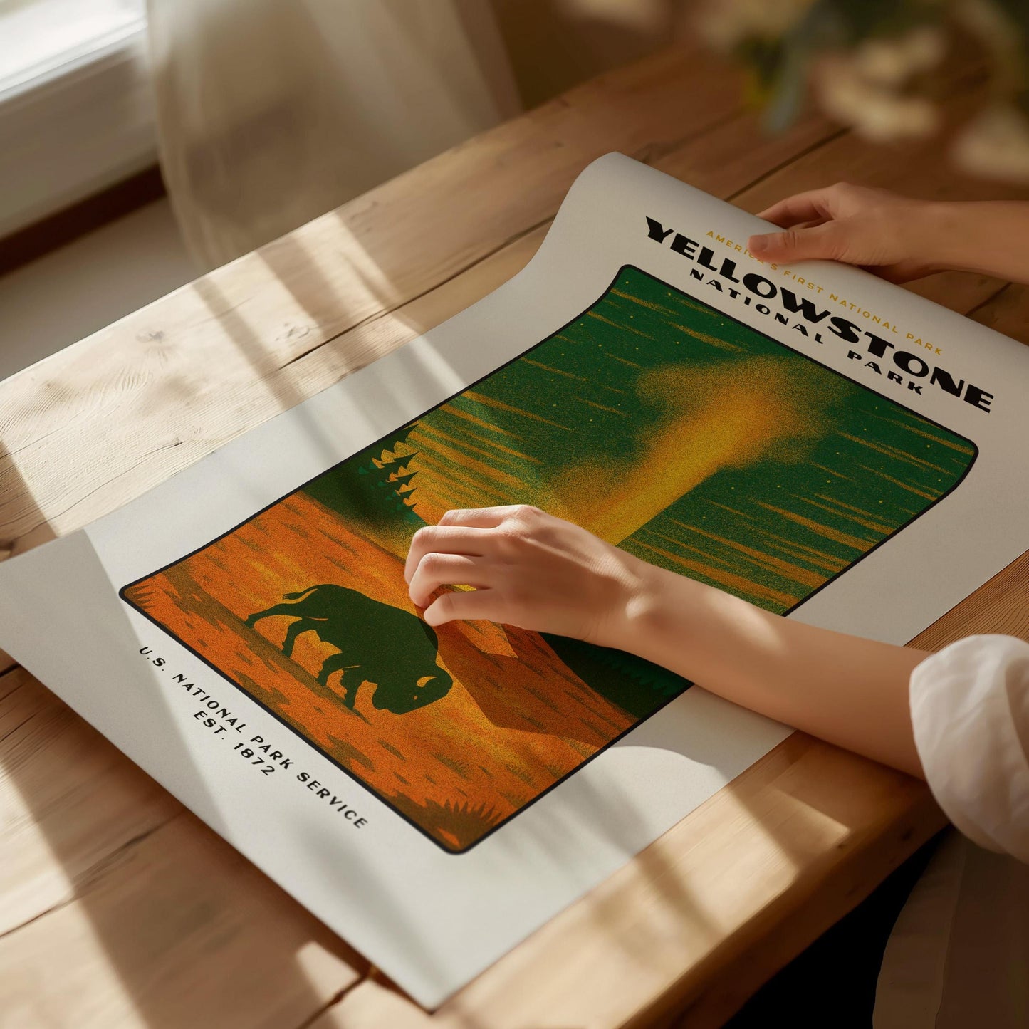 Person holding a Yellowstone National Park poster on a wooden table