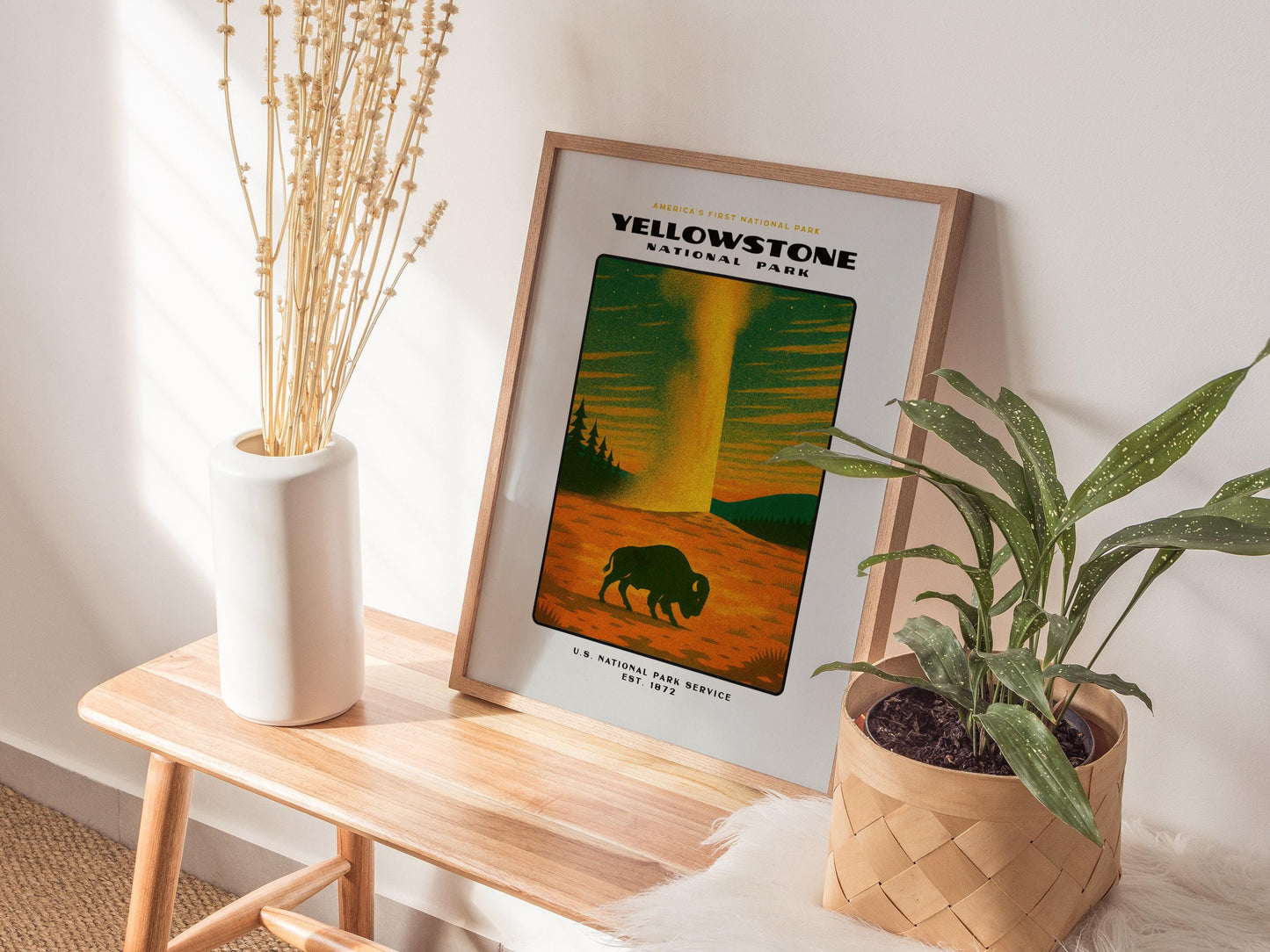 Framed Yellowstone National Park poster on a wooden side table with plants and a vase.