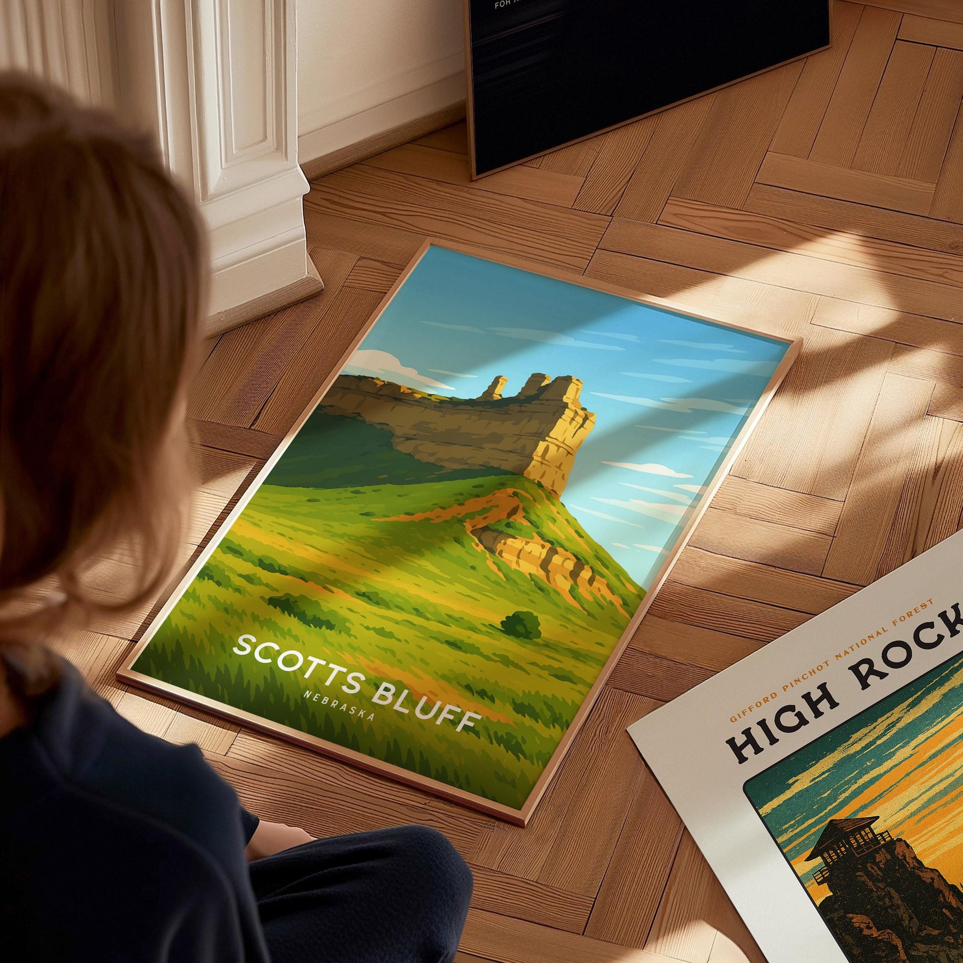 Person looking at a framed poster of Scotts Bluff National Monument on a wooden floor.