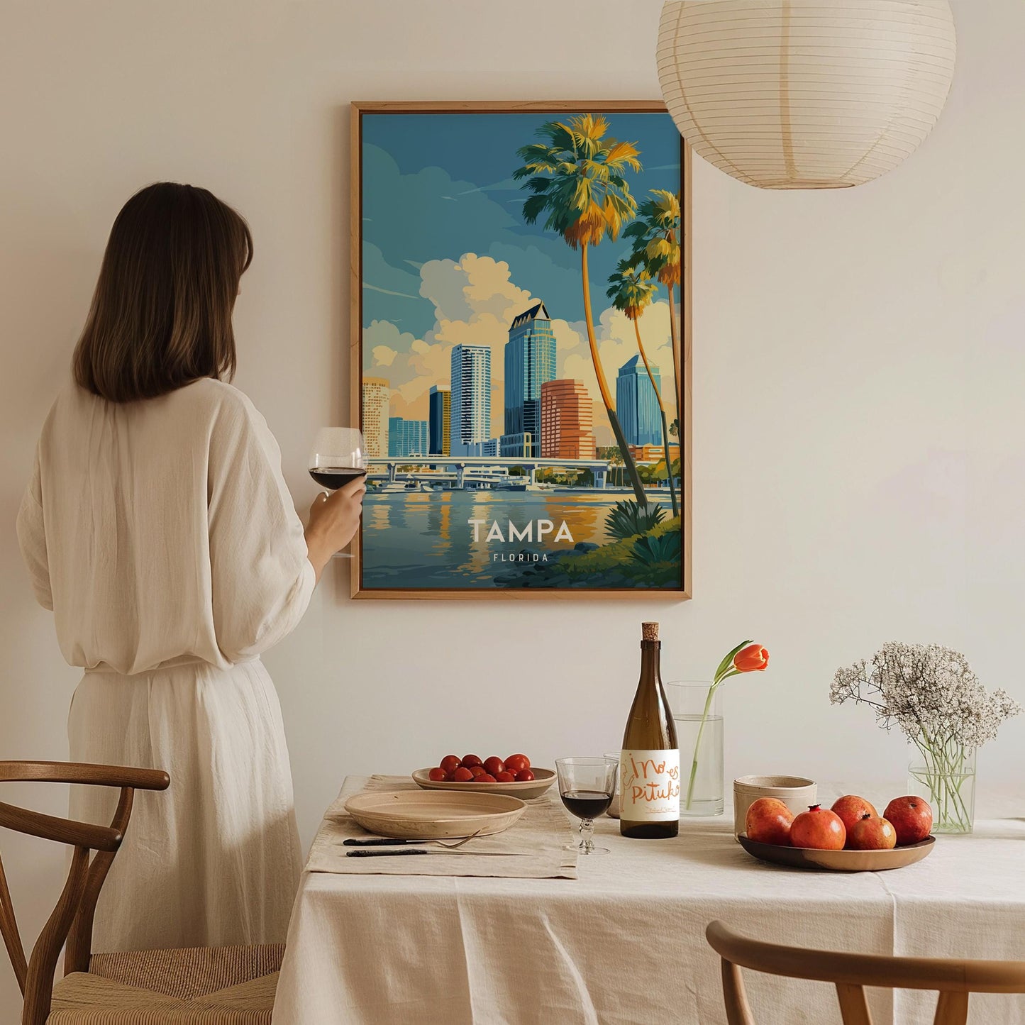 Woman in a white dress standing in a dining room with a framed poster of Tampa, Florida on the wall.