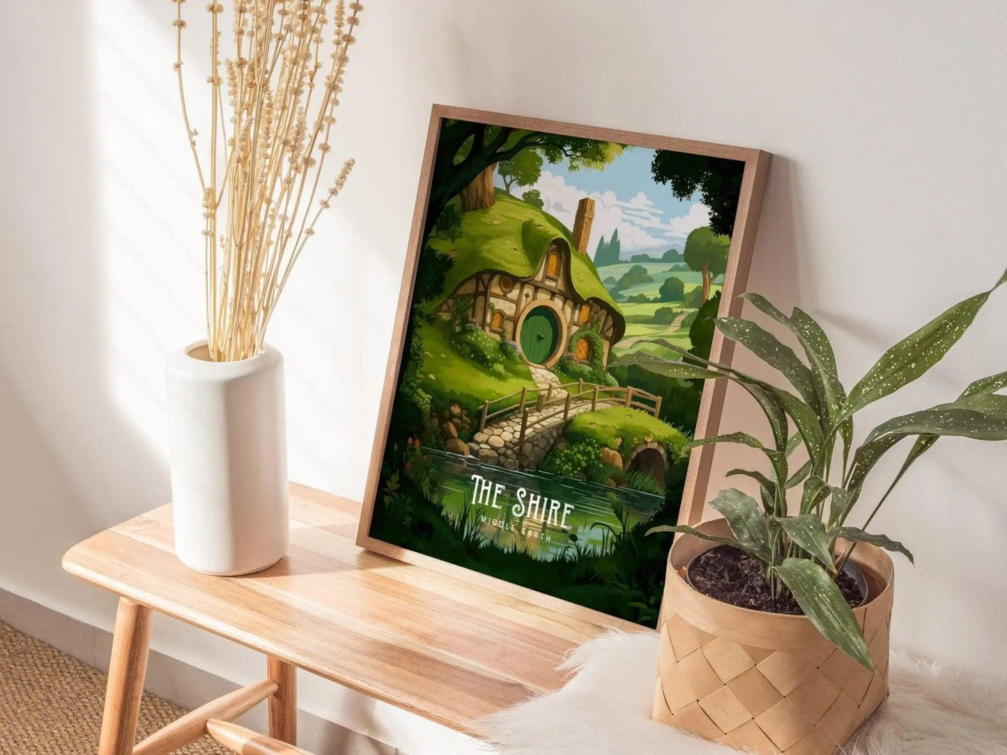 Framed artwork of 'The Shire' from 'The Lord of the Rings' on a wooden table with plants.