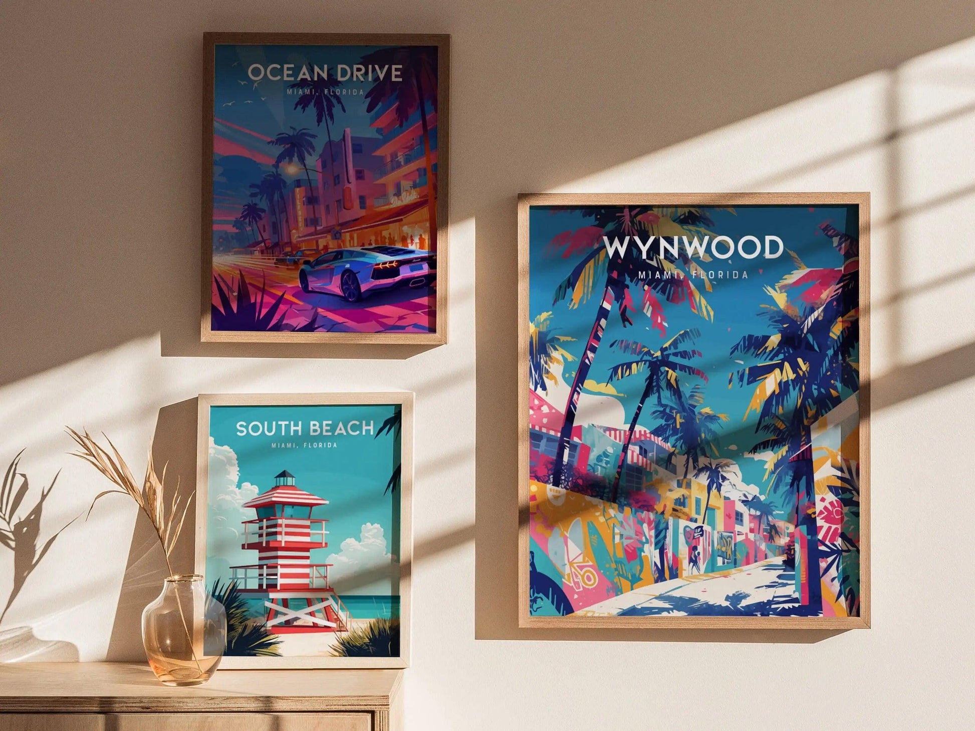 Three framed posters of Miami locations on a wall with sunlight casting shadows.