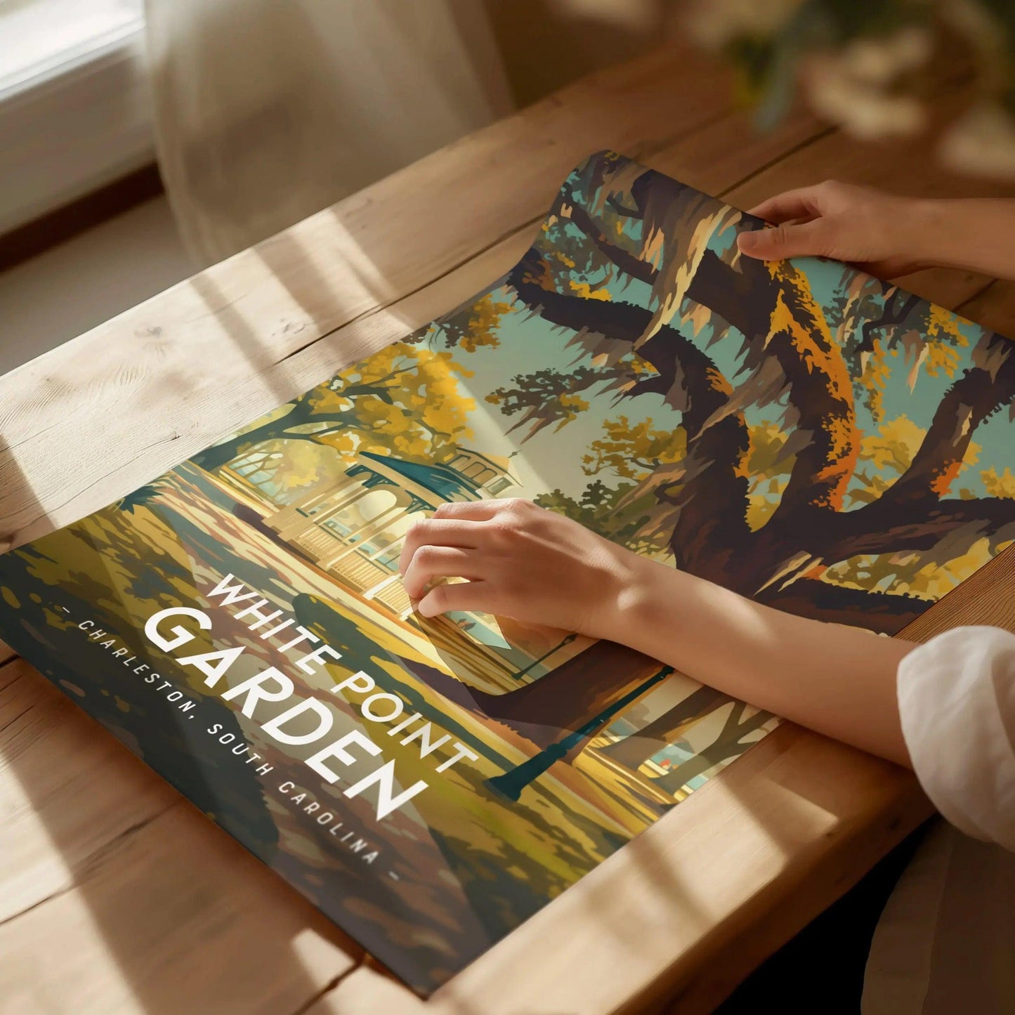Person holding a poster of White Point Garden in Charleston, South Carolina on a wooden table.