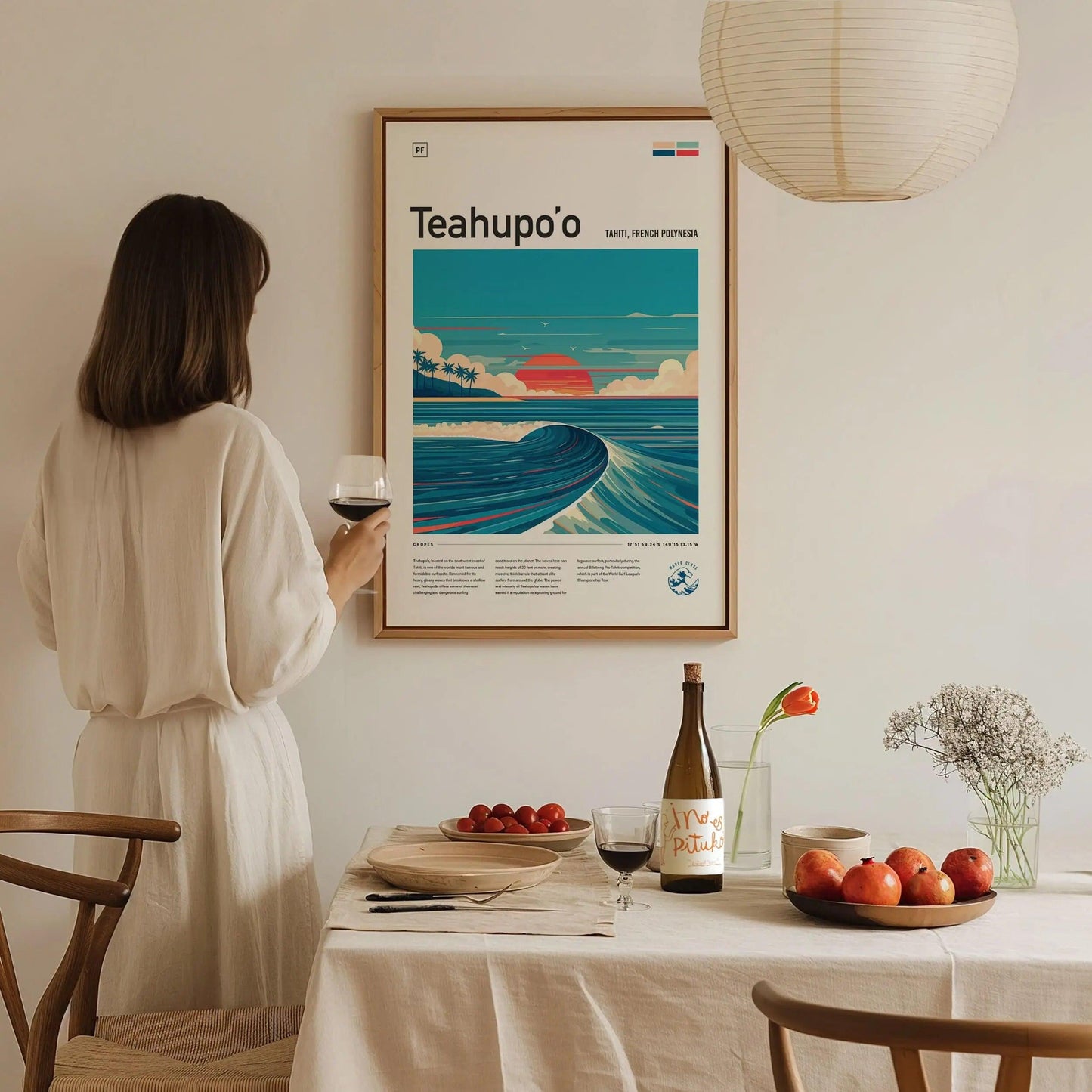 Woman in a white dress standing in a dining room with a framed poster of Teahupo'o.