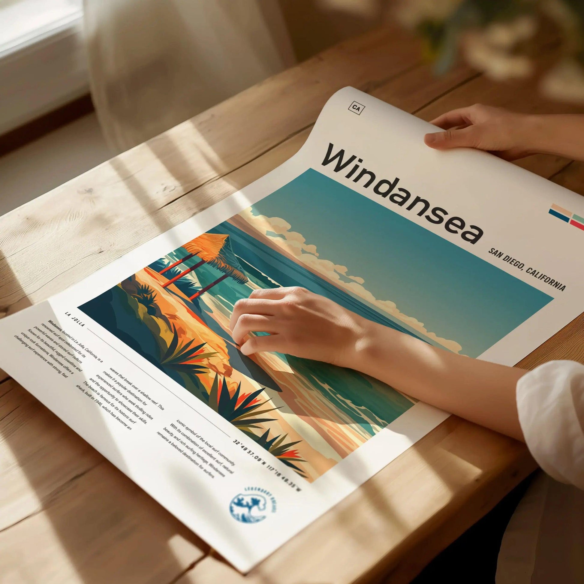 Person holding a poster titled 'Windansea' on a wooden table