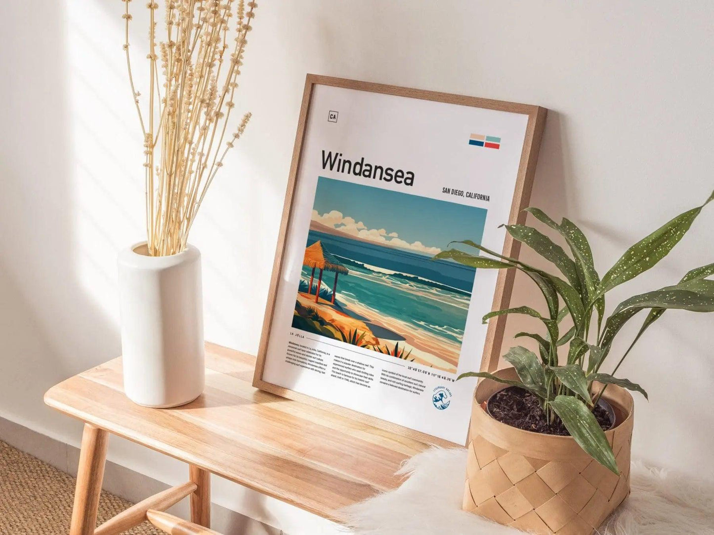 Framed poster of Windansea Beach on a wooden table with plants and a vase.