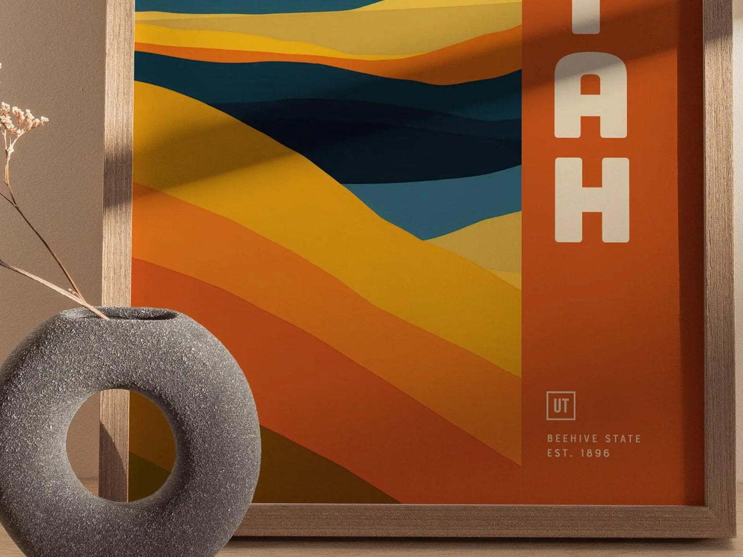 Framed abstract art with geometric design and 'UTAH' branding, next to a textured vase.