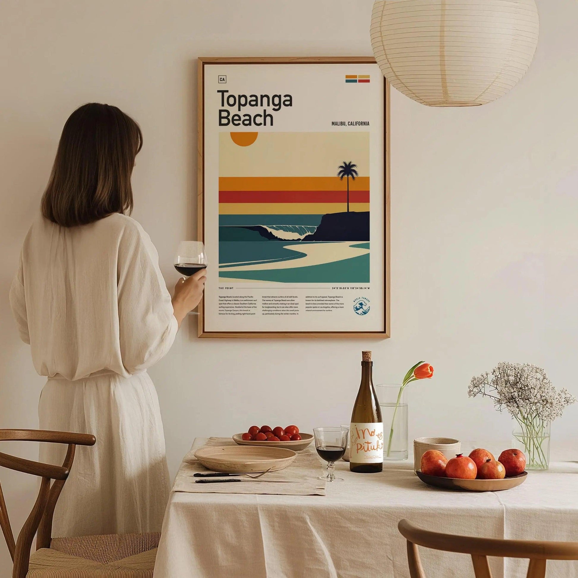 Woman in a white dress standing in a dining room with a framed poster of Topanga Beach.
