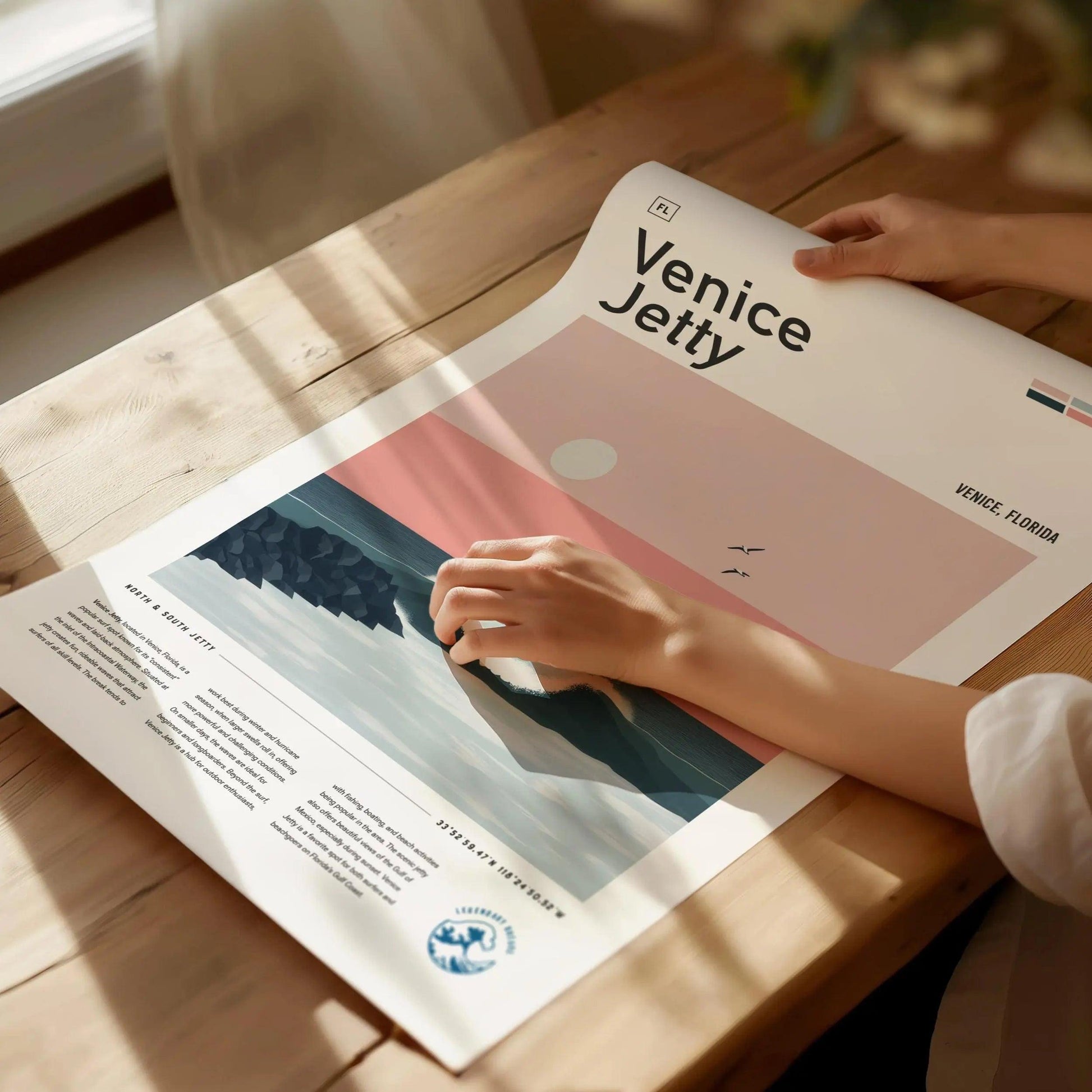 Person holding a poster titled 'Venice Jetty' on a wooden table