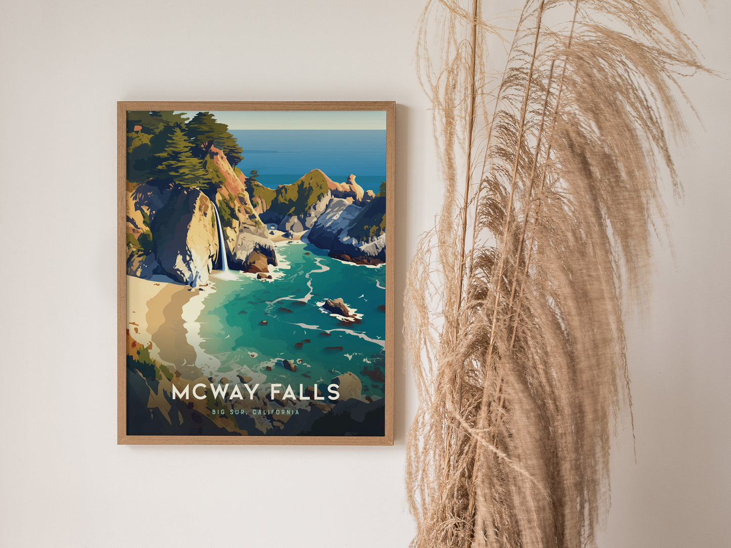 Framed poster of McWay Falls in Big Sur, California, featuring a turquoise cove and rugged cliffs, displayed on a wall beside tall dried grasses.