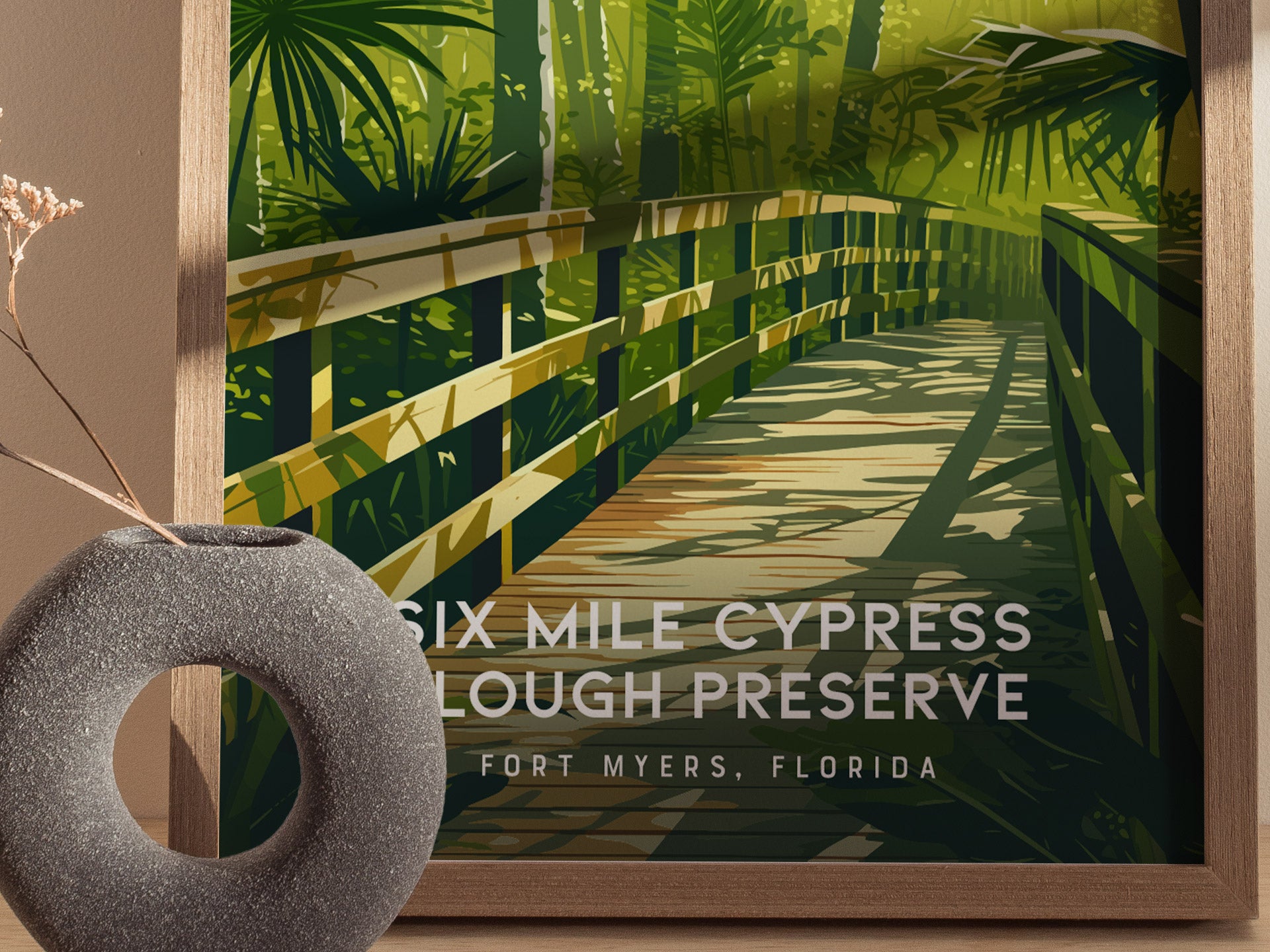 Framed artwork of a wooden boardwalk with greenery, labeled 'Six Mile Cypress Slough Preserve, Fort Myers, Florida', next to a decorative stone object.