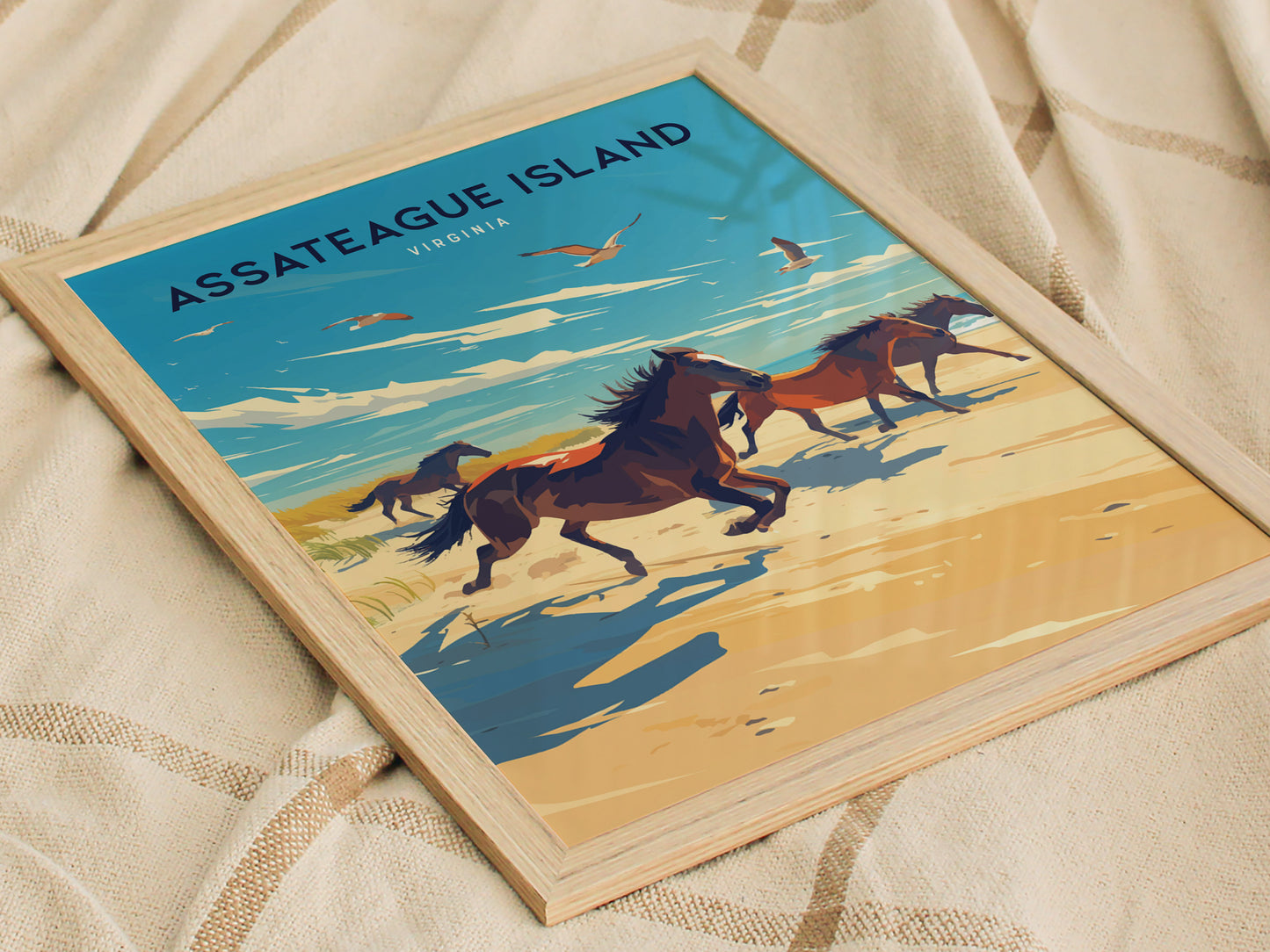 Framed Assateague Island poster featuring wild horses running along a beach with a vibrant sky and seagulls, placed on a soft, textured fabric.