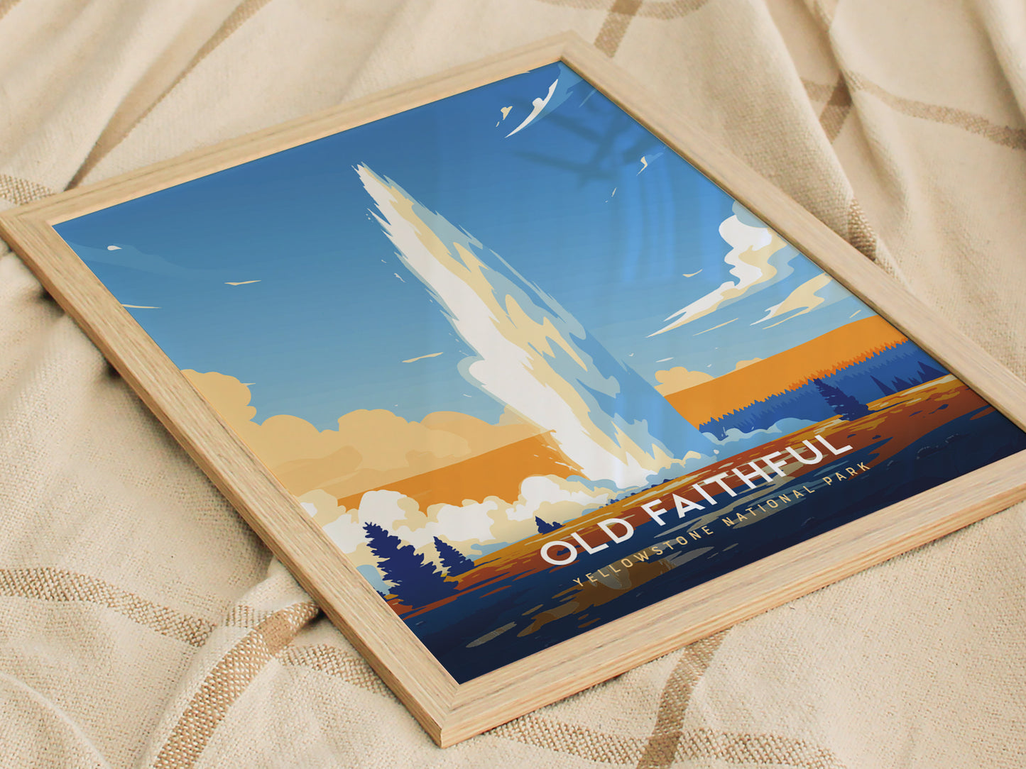 A framed poster of Old Faithful Geyser in Yellowstone National Park, featuring a stylized eruption against a vibrant blue and orange sky, resting on a fabric surface.