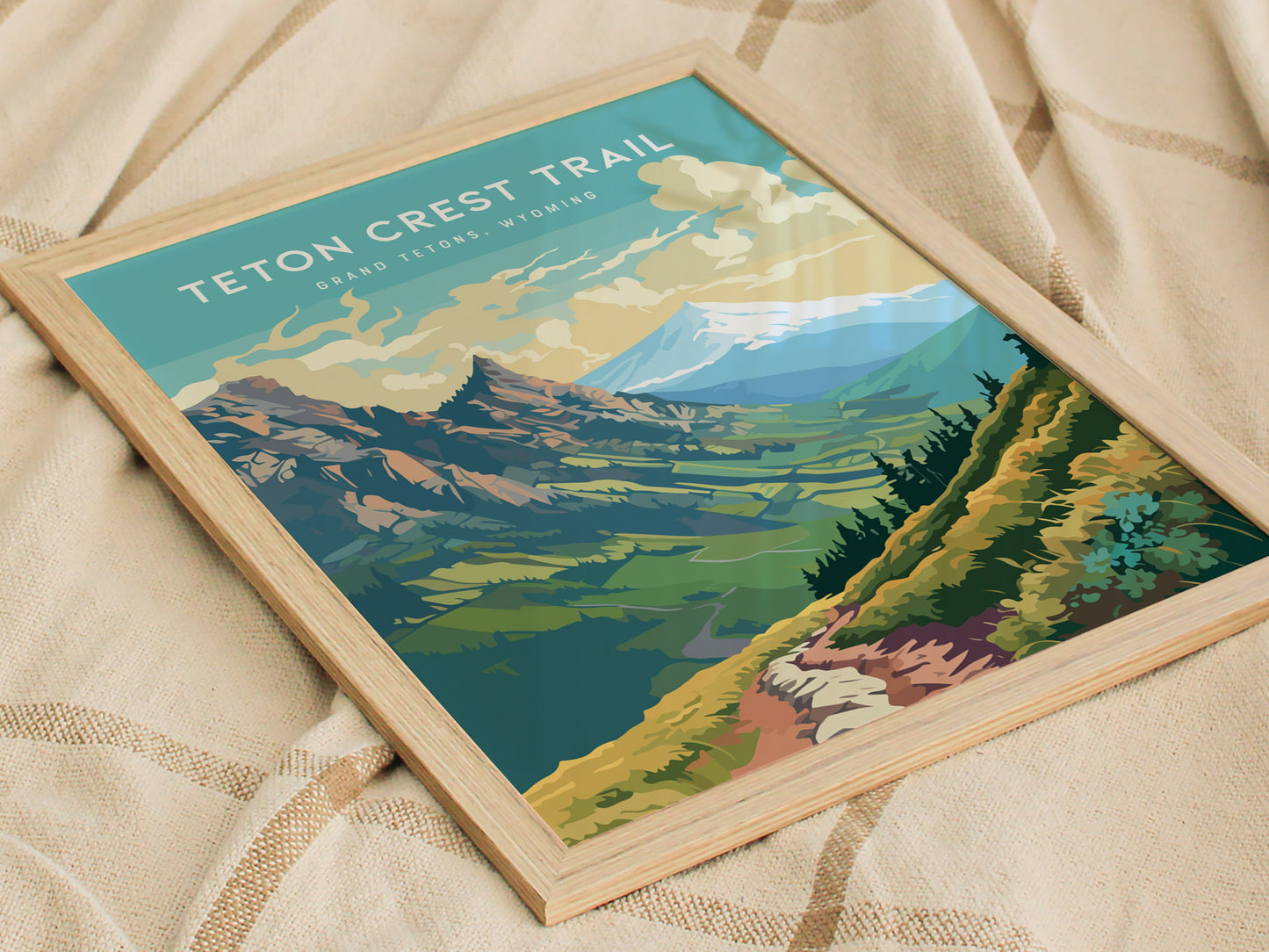 Framed Teton Crest Trail poster with a colorful illustration of mountainous terrain and wildflower meadows, placed on a textured beige fabric surface.