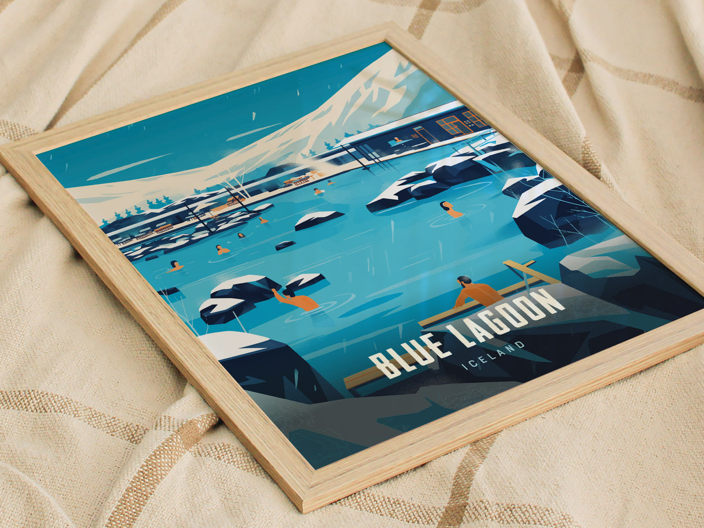 Framed poster of Blue Lagoon, Iceland, featuring people in milky blue geothermal waters surrounded by black lava rocks and snow-capped mountains, resting on a beige fabric background.