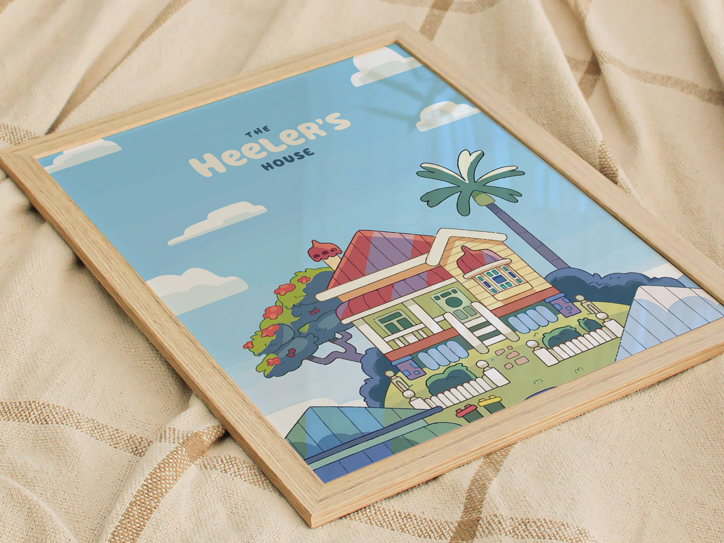 A framed poster depicts a colorful, cartoon-style house with a palm tree and garden, set against a blue sky with clouds. The text reads The Heelers House.