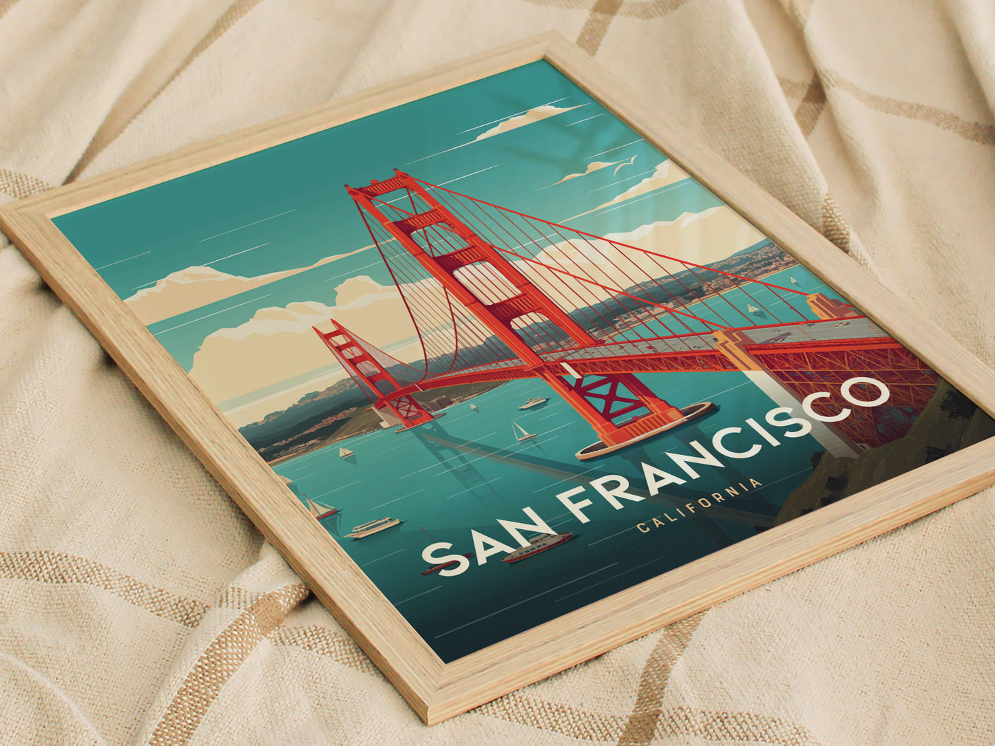 A framed poster of the Golden Gate Bridge with a vibrant blue sky and water, featuring the text San Francisco California, resting on a textured beige fabric.