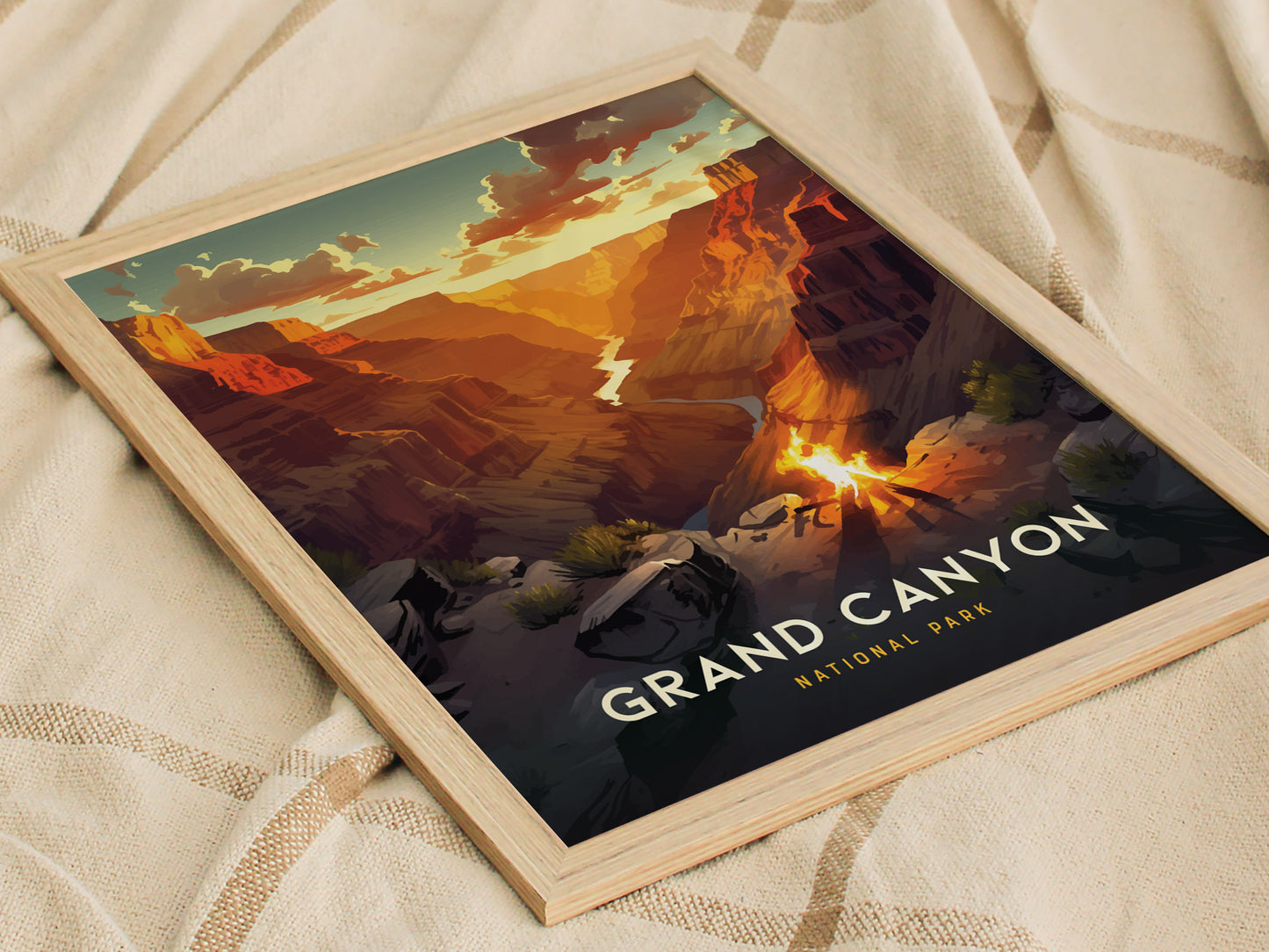 A framed poster of the Grand Canyon features a vibrant sunset over layered rock formations, with the text Grand Canyon National Park visible. The poster rests on a beige fabric.