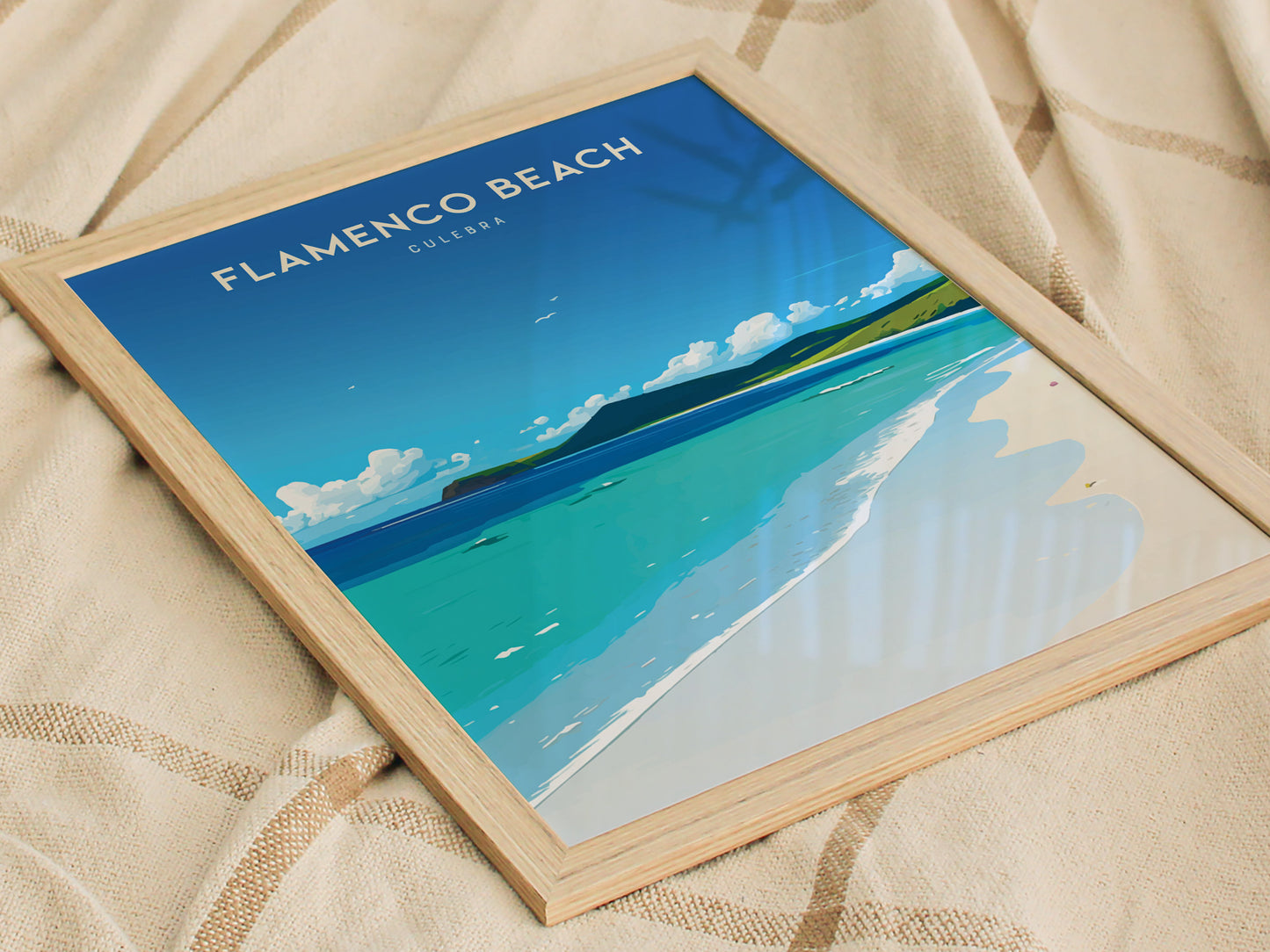 Framed poster of Flamenco Beach, Culebra, featuring a serene beach scene with turquoise waters and a clear blue sky, resting on a beige fabric surface.