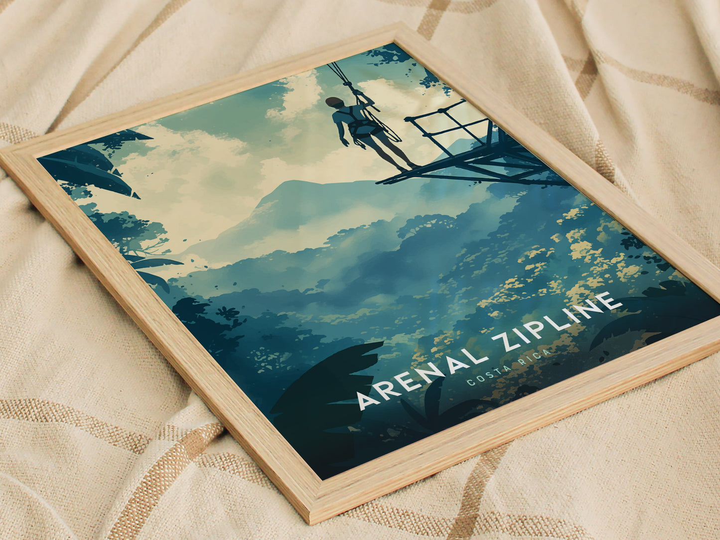 A framed poster on a beige fabric background depicts a person ziplining through a lush, mountainous landscape with Arenal Zipline Costa Rica text at the bottom.