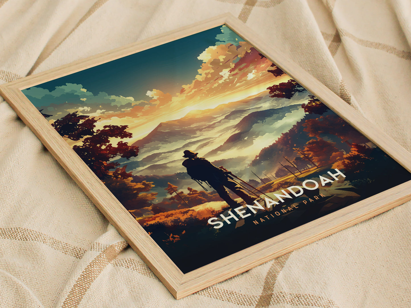A framed poster depicting a vibrant landscape of Shenandoah National Park with a silhouetted figure overlooking rolling mountains and colorful skies at sunset. The poster rests on a textured fabric.