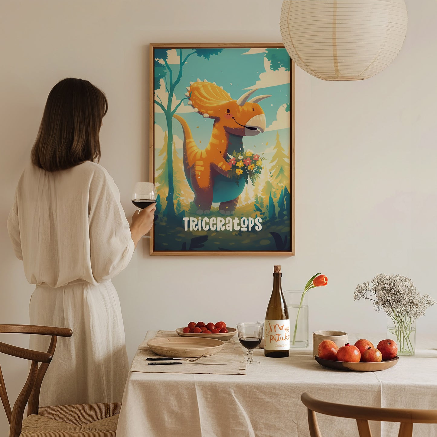 A woman in a white dress admires a colorful triceratops poster in a dining room. The table is set with wine, fruit, and flowers, creating a cozy atmosphere.
