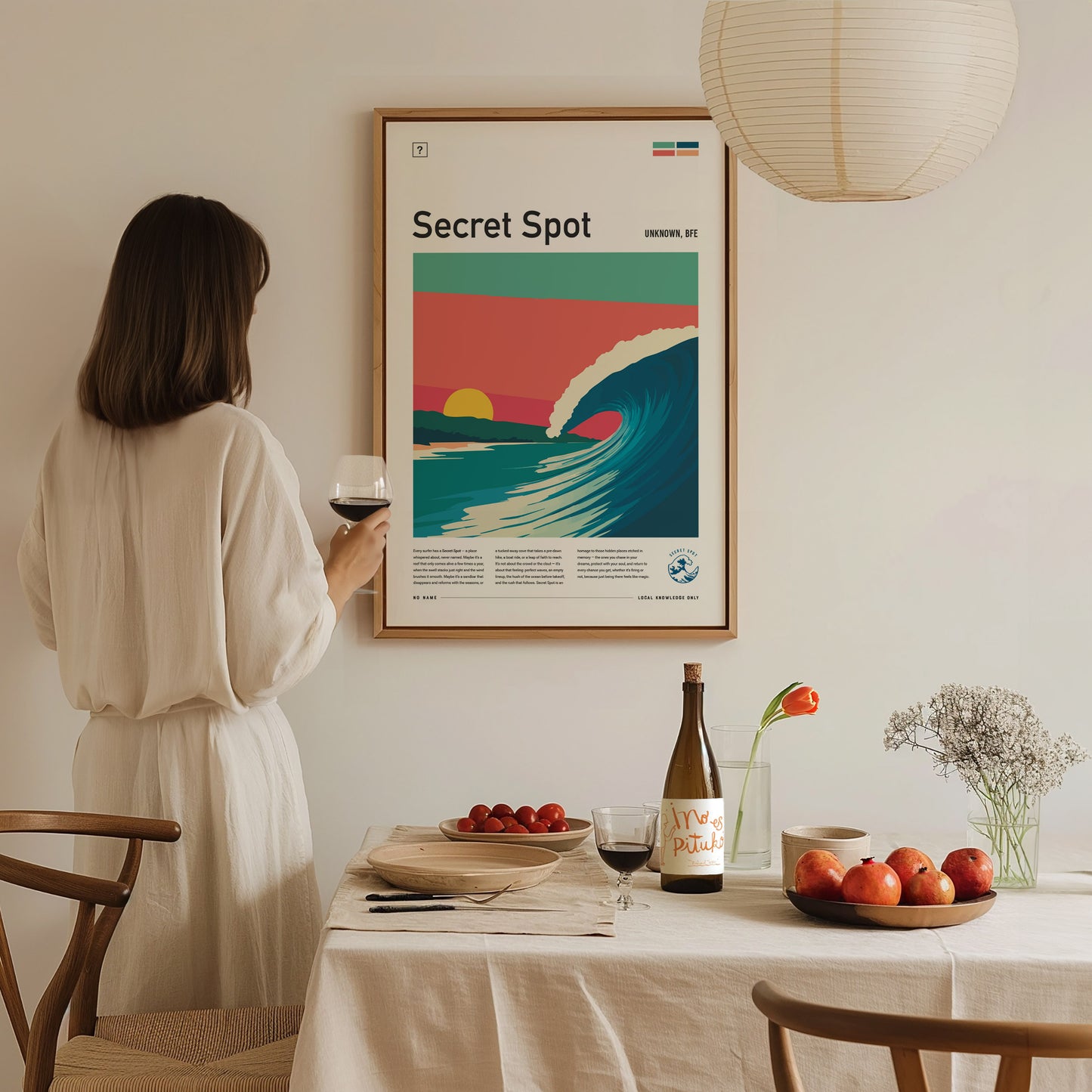 A woman in a cream-colored outfit stands in front of a framed poster titled Secret Spot, featuring a vibrant wave under pastel skies.