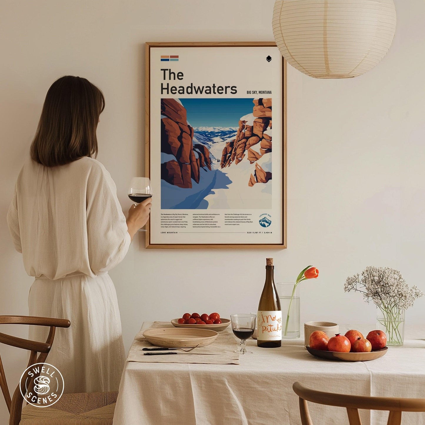 Woman in a white dress standing in a dining room with a 'The Headwaters' poster on the wall.