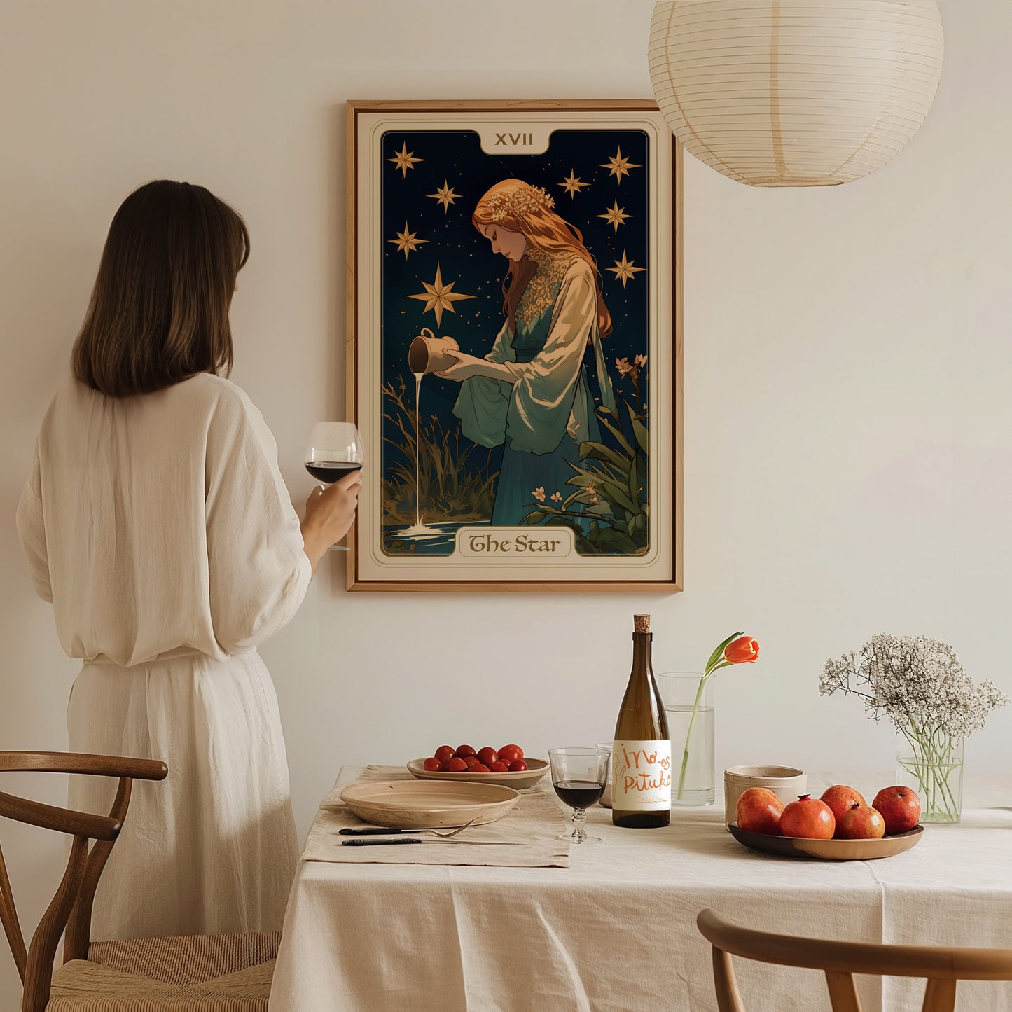 A woman in a white dress holds a glass of wine, admiring a framed Star Tarot Card poster on the wall.