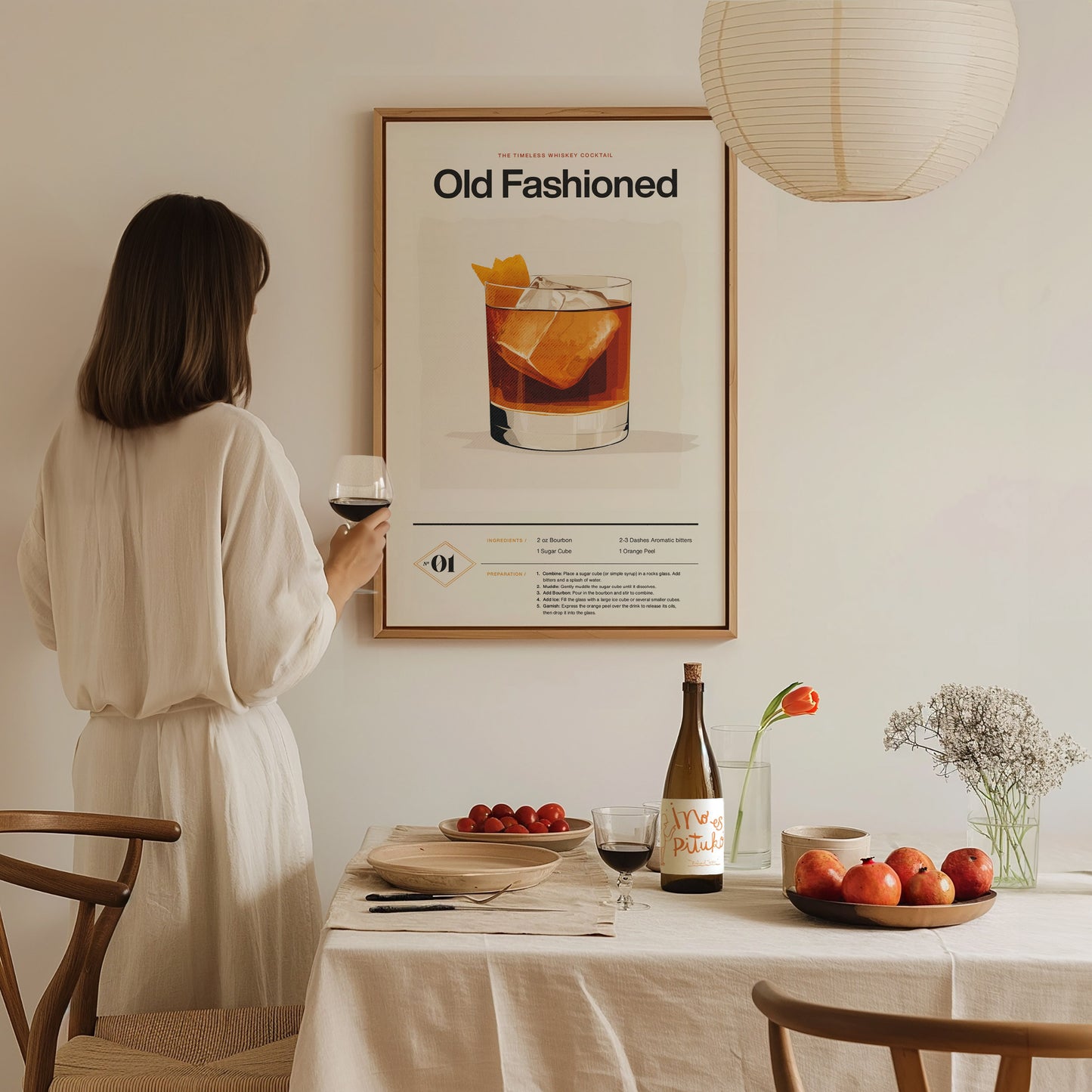 A woman in a white dress holds a glass of wine, looking at an Old Fashioned cocktail poster. A table with fruit, wine, and flowers is in the foreground.