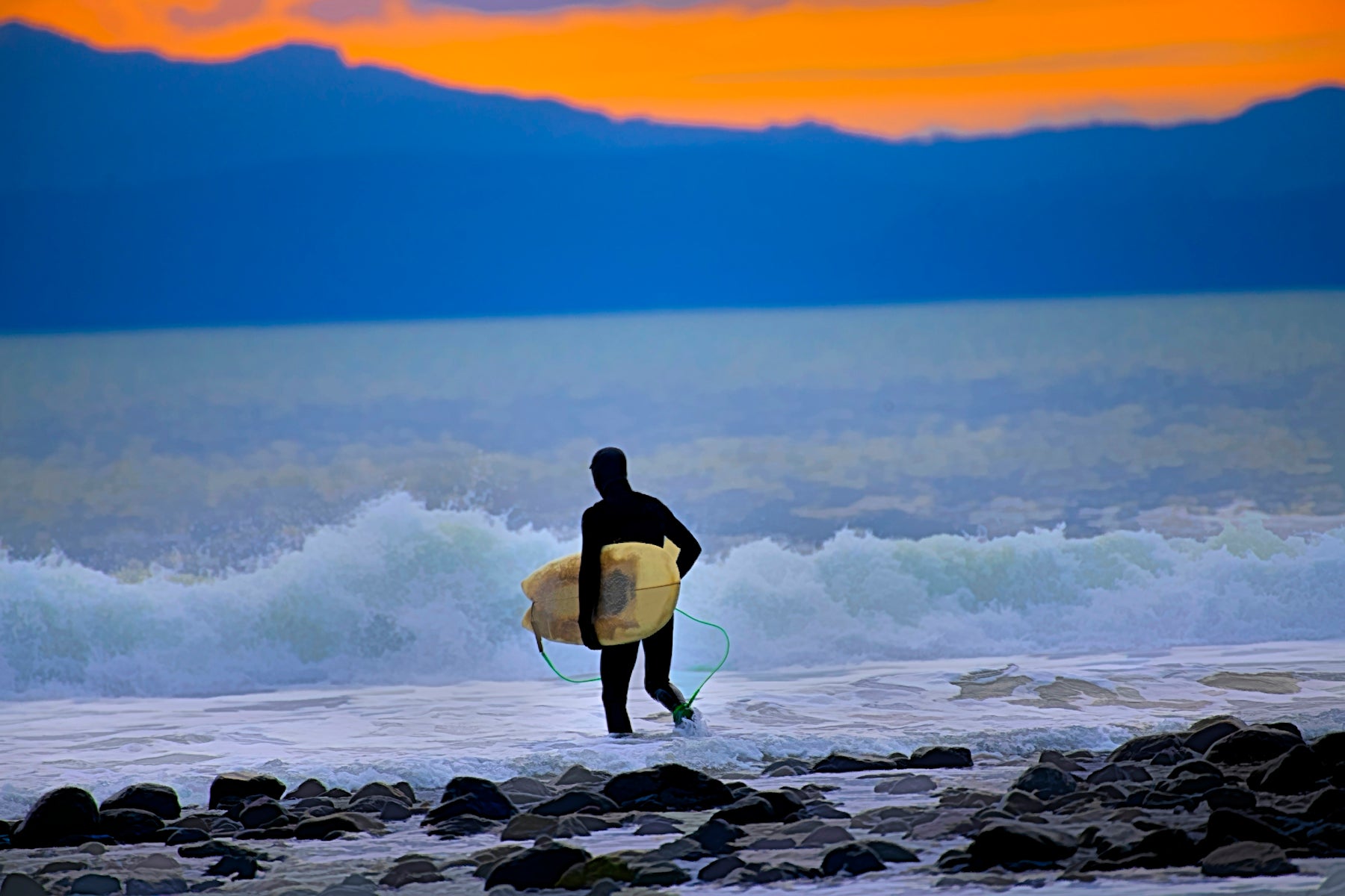 a man holding a surfboard while standing on a rocky beach