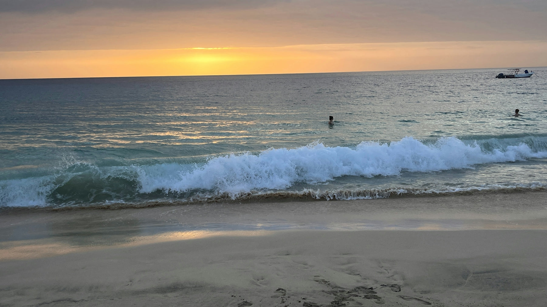 The sun is setting over the ocean with people in the water