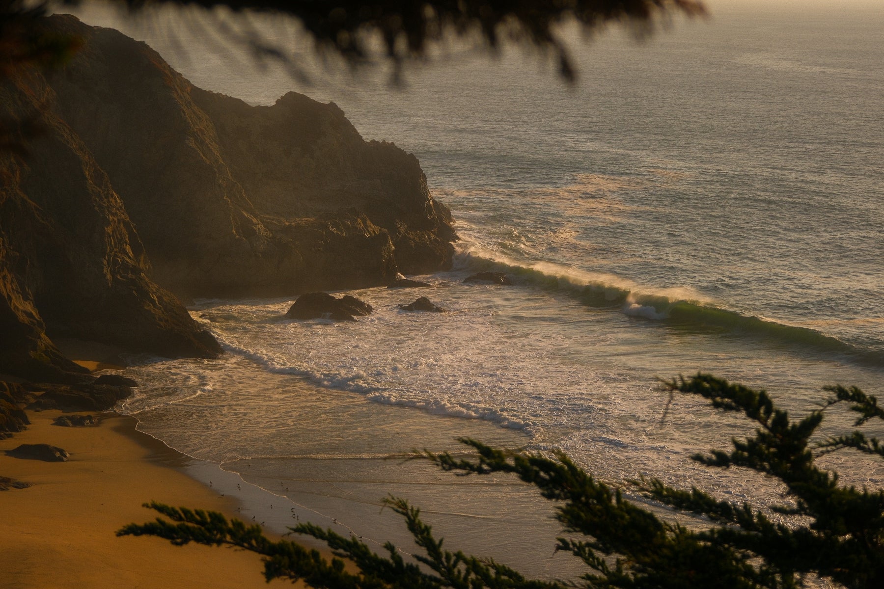 Ocean waves crash on a sandy beach near cliffs.