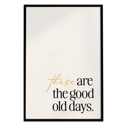 A framed poster features the inspirational quote these are the good days. in a mix of modern typography, with the words these in a flowing cursive style and the rest in bold black letters, all set against a plain white background.