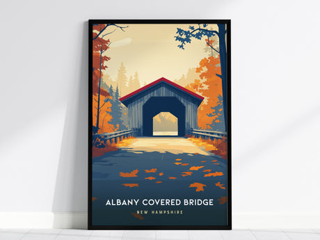 A framed poster of the Albany Covered Bridge in New Hampshire showcases the iconic structure set against a backdrop of vibrant autumn foliage in warm hues of orange, red, and yellow.