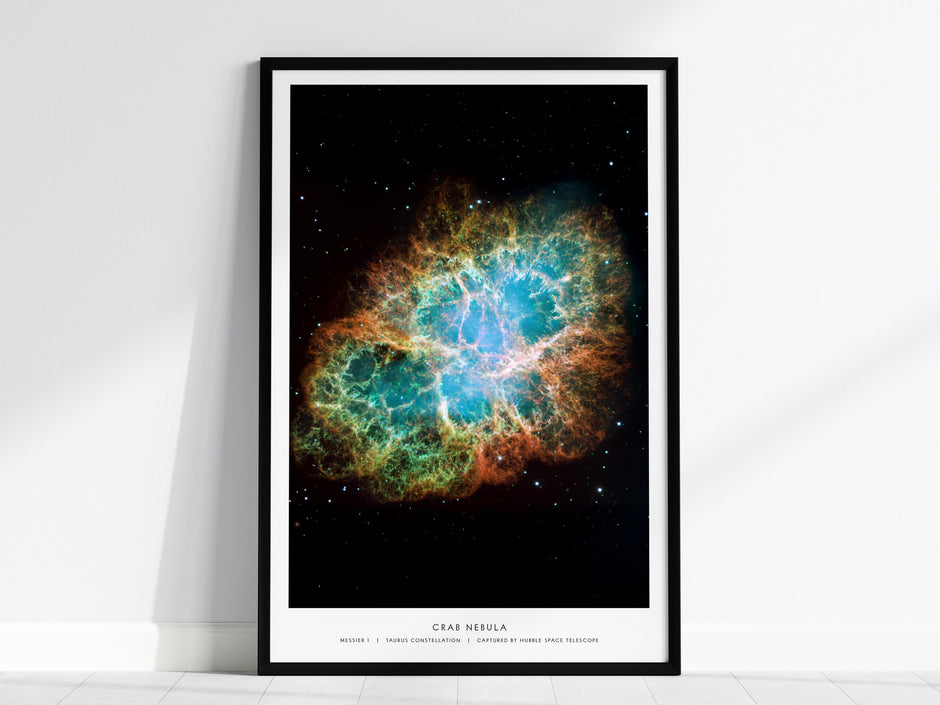 Framed Crab Nebula poster leaning against a white wall, showing vibrant blue and orange supernova remnant on a black star field.