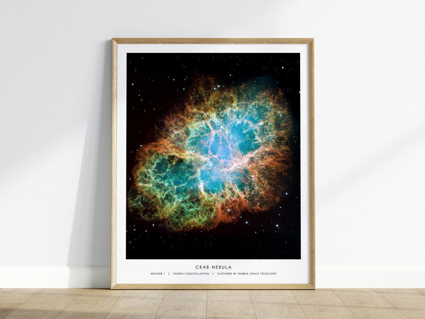 Crab Nebula wall art in a light wood frame on a floor, featuring detailed filaments of glowing gas against deep space.