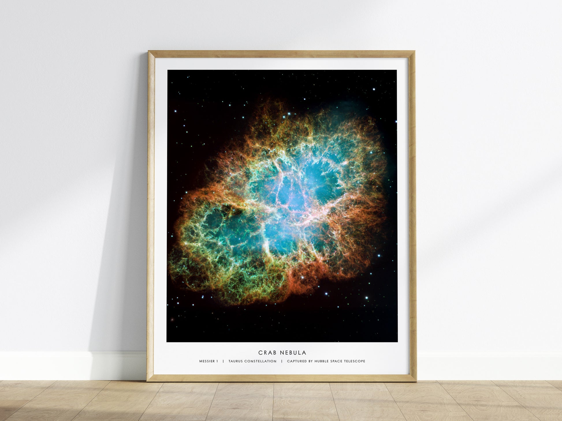 Crab Nebula wall art in a light wood frame on a floor, featuring detailed filaments of glowing gas against deep space.