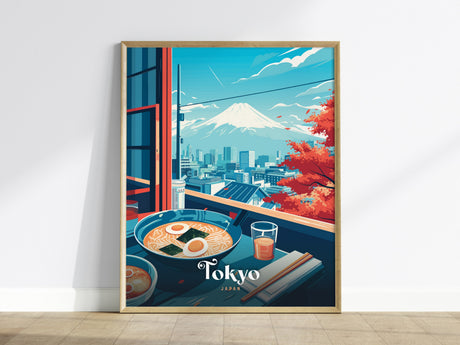 A framed poster depicts a vibrant Tokyo cityscape with Mount Fuji in the background, viewed from a window with a bowl of ramen, chopsticks, and a drink on a table. Red autumn leaves add color to the scene.