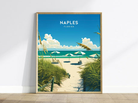 A framed poster of Naples, Florida, featuring a vibrant beach scene with umbrellas, a sandy path, tall grasses, and a bright blue sky with fluffy clouds.