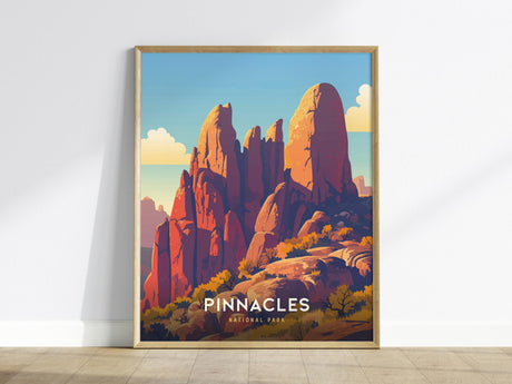 A framed poster featuring an illustration of Pinnacles National Park, showcasing dramatic rock spires and a vibrant landscape under a clear blue sky. The text Pinnacles National Park is visible at the bottom.