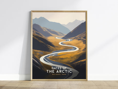 This image shows a framed poster of Gates of the Arctic National Park, featuring a winding river through mountainous terrain in a minimal vector style. The artwork is propped against a white wall on a wooden floor.