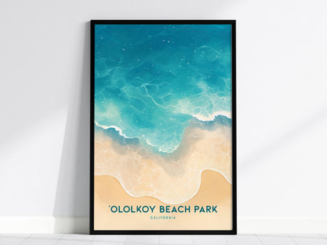 Framed poster depicting a stylized aerial view of a beach with turquoise waves lapping against sandy shores. Text at the bottom reads Ololkoy Beach Park, California. The poster is set against a plain white wall.