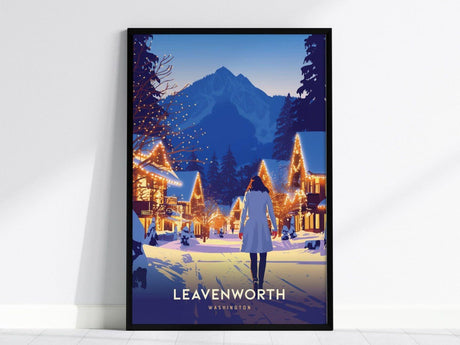 A framed poster depicting a snowy village street in Leavenworth, Washington, with a person walking toward illuminated buildings and mountains in the background.
