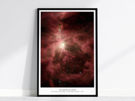 A framed poster of the Orion Nebula features swirling red and pink cosmic clouds with a bright central light, set against a black space backdrop. The poster is titled The Sword of Orion and leans against a white wall.