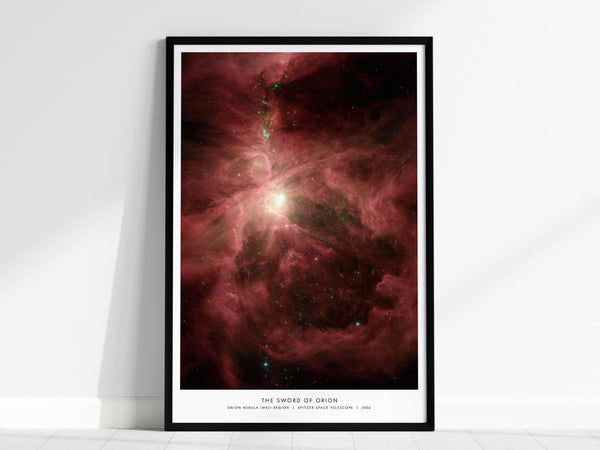 A framed poster of the Orion Nebula features swirling red and pink cosmic clouds with a bright central light, set against a black space backdrop. The poster is titled The Sword of Orion and leans against a white wall.