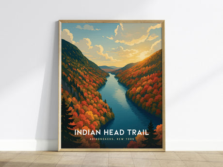 The image shows a framed poster of the Indian Head Trail in the Adirondacks, New York, featuring a vibrant autumn landscape with colorful trees and a river under a dramatic sky at sunset. The poster leans against a white wall.