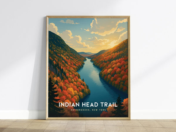 The image shows a framed poster of the Indian Head Trail in the Adirondacks, New York, featuring a vibrant autumn landscape with colorful trees and a river under a dramatic sky at sunset. The poster leans against a white wall.