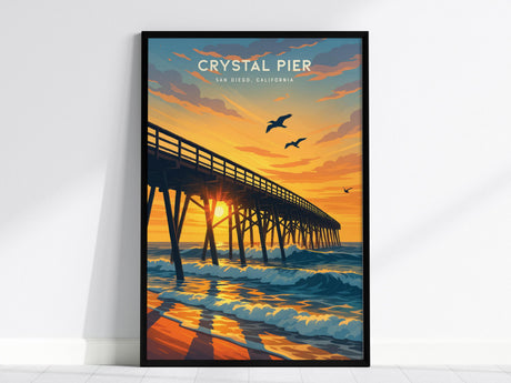 A framed poster of Crystal Pier in San Diego features a sunset with vivid orange and blue hues. Seagulls soar above the waves, and the sun casts shadows through the piers wooden beams.